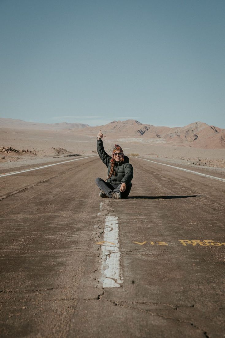 Ricardo Cardoso sentado no meio de uma estrada no deserto do Atacama, acenando