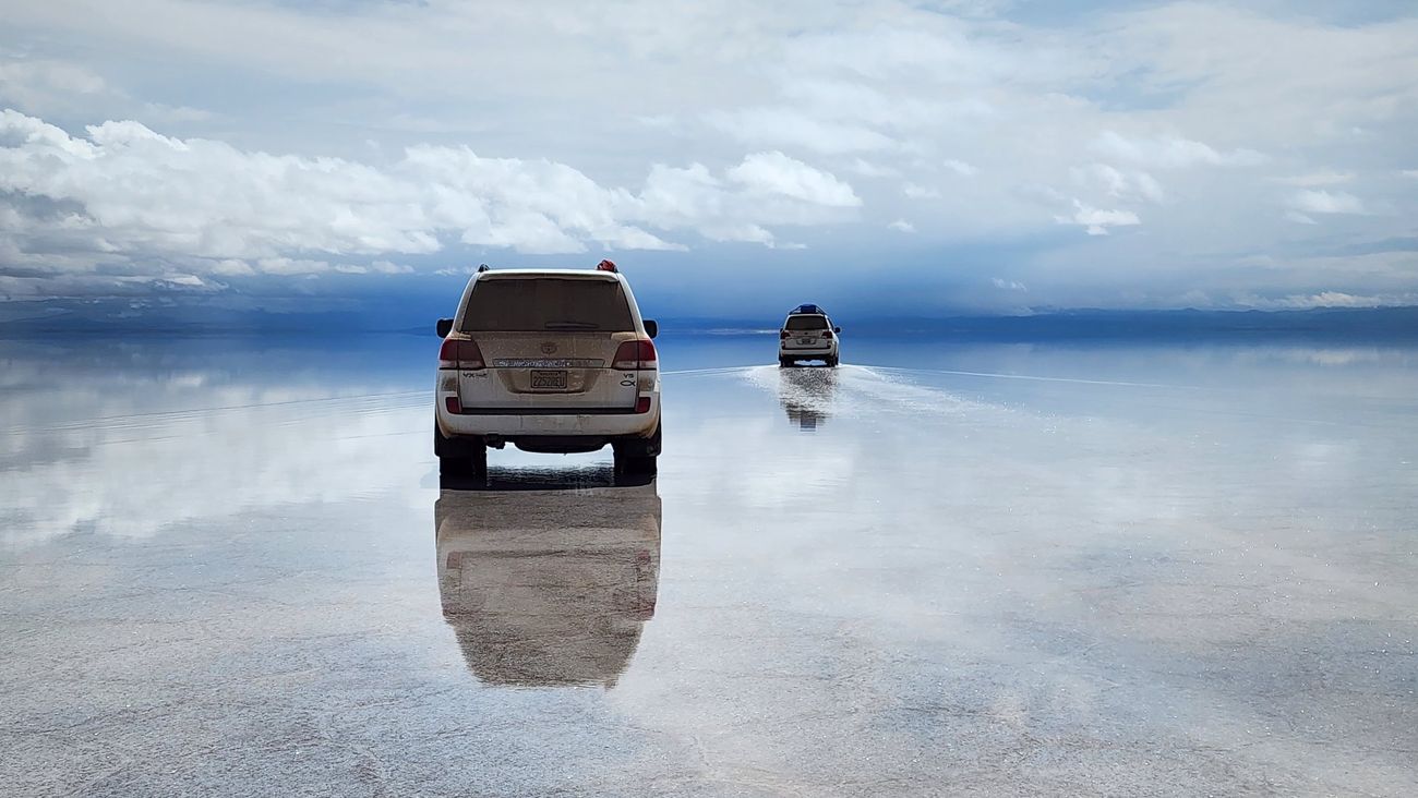 Dois carros 4x4 atravessando o Salar de Uyuni coberto de água, refletindo o céu
